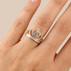 Hand wearing a ring with a crown design on a neutral background