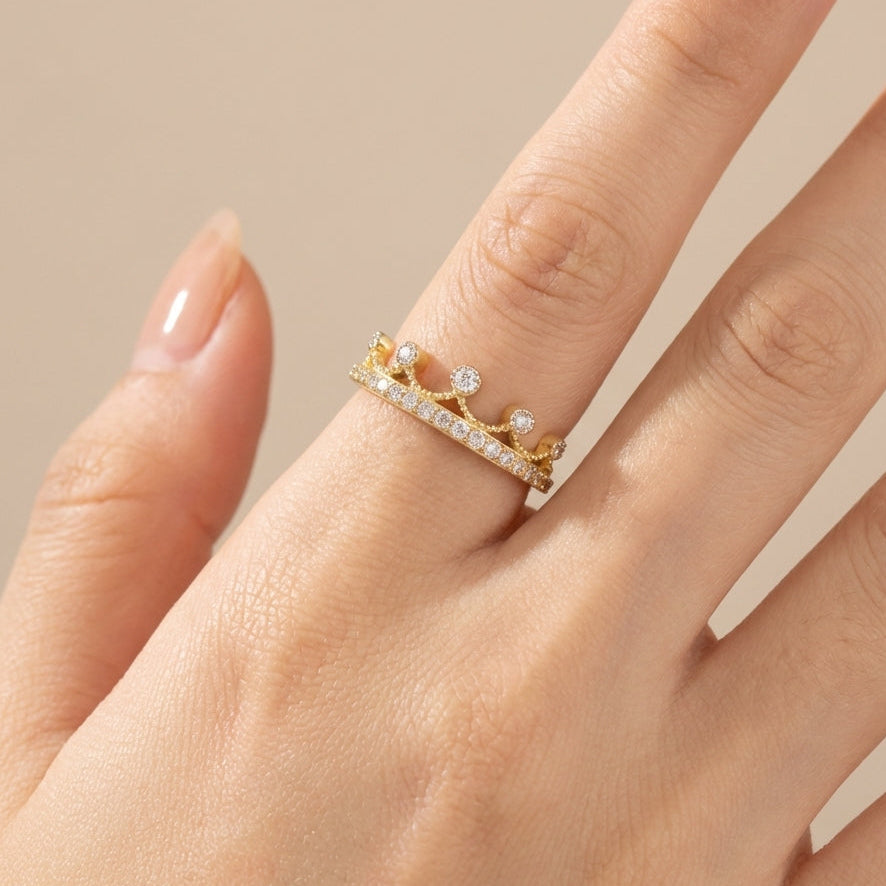Gold ring with small diamonds on a hand against a beige background