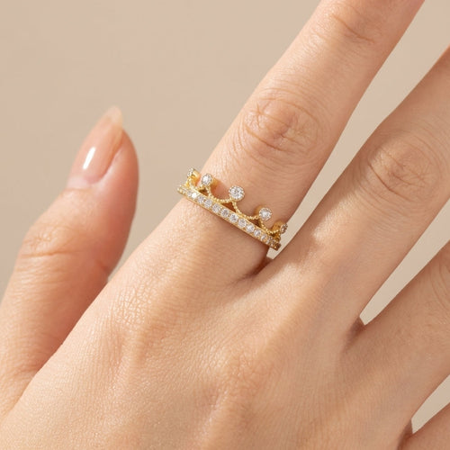 Gold ring with small diamonds on a hand against a beige background