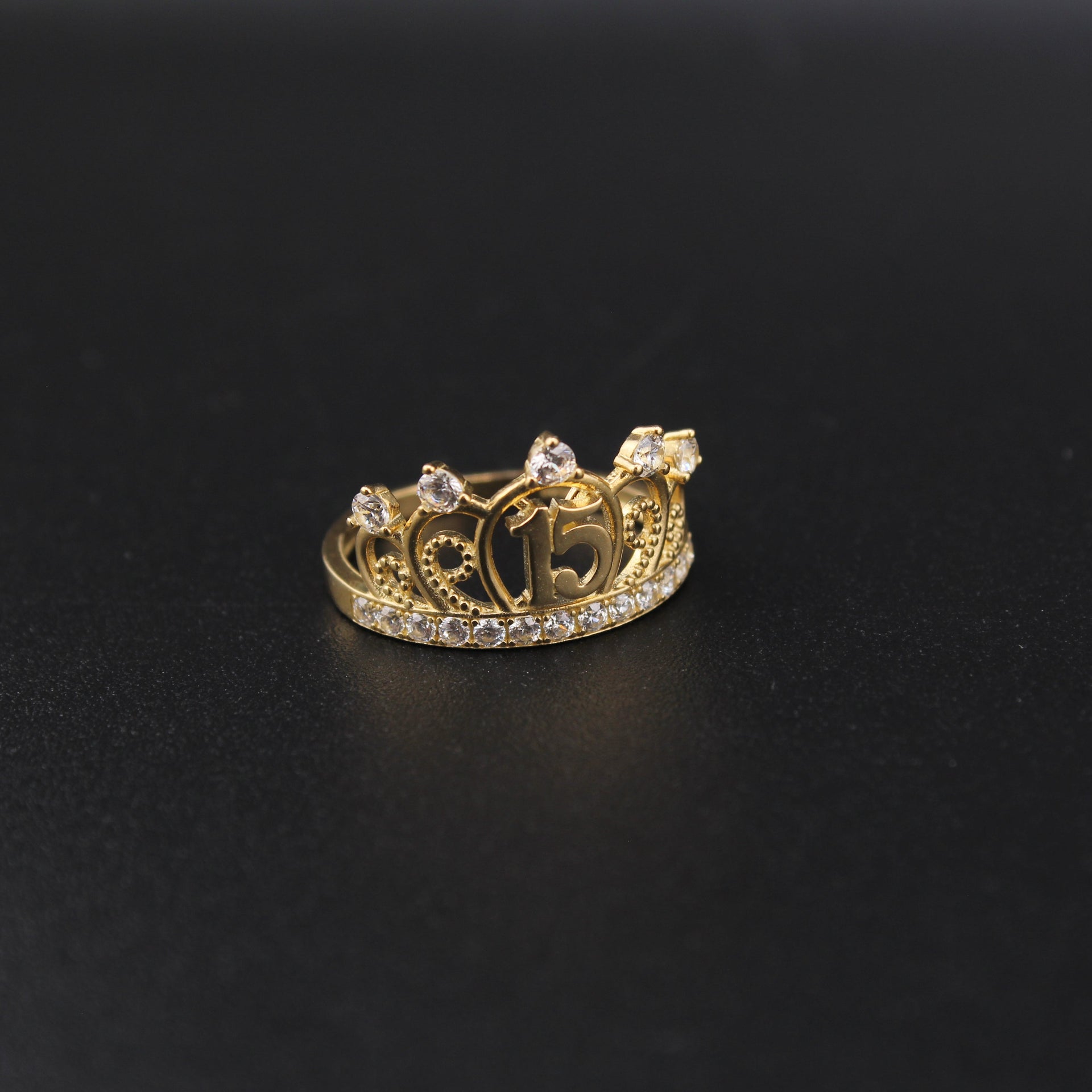 Gold crown-shaped ring with gemstones on a black background